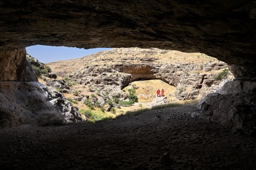 Grotte de Gugurtli (Turkménistan) - Porche d'entrée vu de l'intérieur avec deux spéléologues sur un rocher à l'extérieur(SP-26-0583)