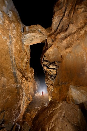 Cueva Canuela (Cantabrie, Espagne) - Galerie de l'arche : bloc perché au dessus d'une galerie avec personnage  contre jour en fond.(SP-26-1007)