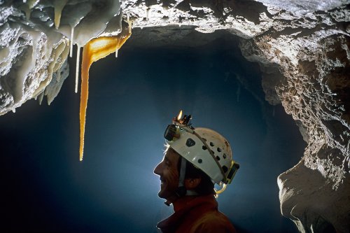 Aven des Crozes (Hérault) - Spéléo contre-jour de profil regardant une stalactite jaune(Spe-06411)