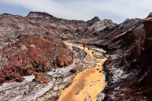Iran (île d'Hormoz) - randonneuse dans vallée de Rangin Kaman progressant dans rivière à sec couverte de dépôts jaunes au milieu sel rouge(VO-16-0207)