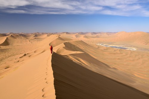 Désert du Badain Jaran (Chine, Mongolie Intérieure) - Vue générale d'un enchaînement de grandes dunes avec randonneuse sur la crête. Vallée avec lac salé à droite.(VO-16-0948)