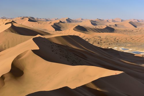 Désert du Badain Jaran (Chine, Mongolie Intérieure) - Vue générale d'un enchaînement de grandes dunes avec randonneuse au loin sur la crête. Vallée avec lac salé à droite.(VO-16-0987)