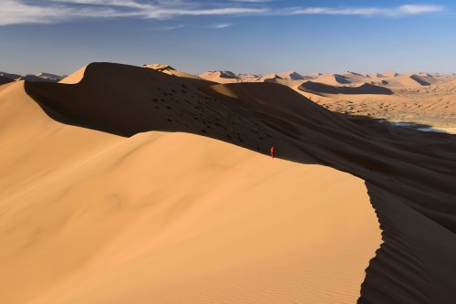 Désert du Badain Jaran (Chine, Mongolie Intérieure) - Vue générale d'un enchaînement de grandes dunes avec randonneuse au loin sur la crête. un versant éclairé par le soleil couchant et un versant à l'ombre (VO-16-1003)