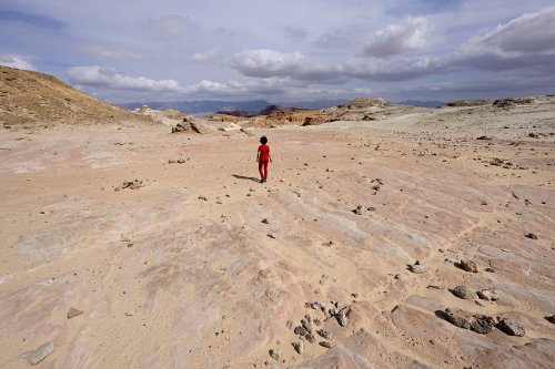 Parc national de Timna (Israël) - Personnage sur grand espace plat caillouteux désertique au pied des arches (VO-23-0275)