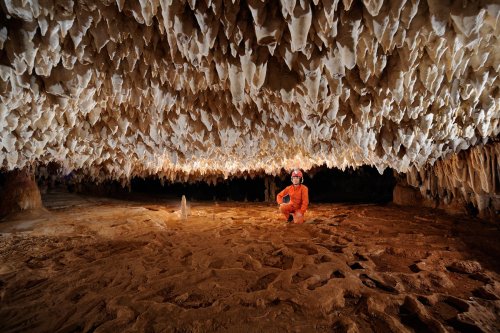 Cueva de Santa Catalina (Expédition Cuba 2012 - Team La Salle). Spéléo accroupi dans galerie au plafond bas concrétionné. (SP-12-0010)