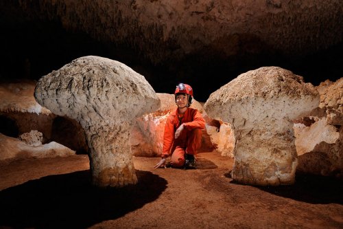 Cueva de Santa Catalina (Expédition Cuba 2012 - Team La Salle). Spéléo  accroupie entre deux concrétions en forme de champignons.(SP-12-0027)