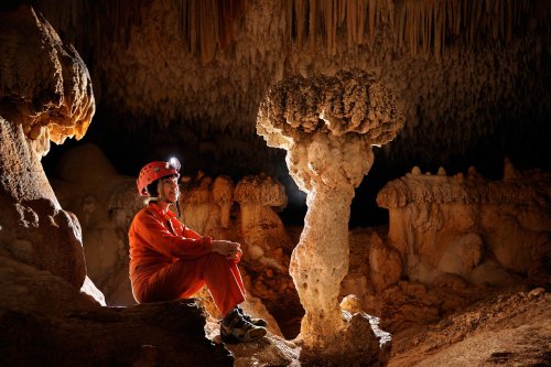 Cueva de Santa Catalina (Expédition Cuba 2012 - Team La Salle). Spéléo assise entre  deux  concrétions en forme de champignons.(SP-12-0071)