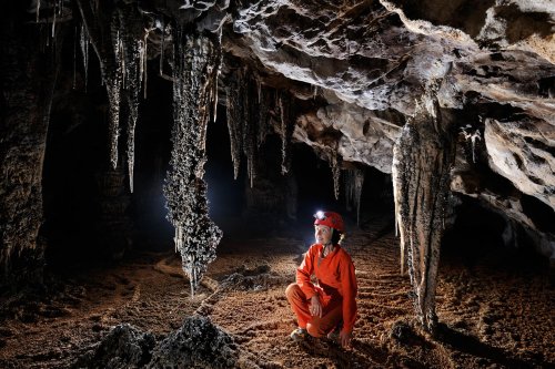 Cueva de Santo Tomas Expédition Cuba 2012 - Team La Salle. Galerie avec spéléo accroupie devant deux concrétions grises massives.(SP-12-0212)