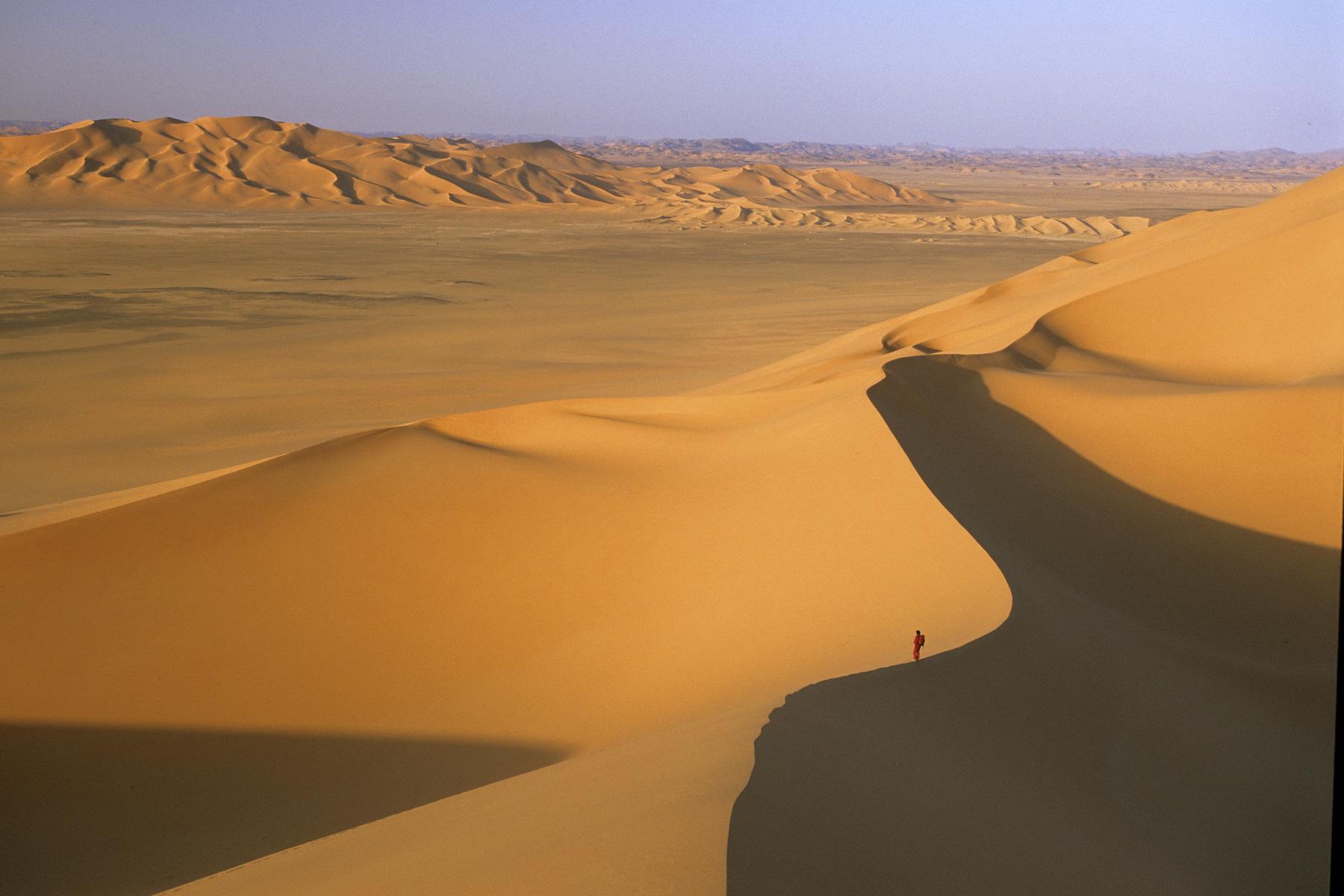 Femme (silhouette rouge) progressant sur la crête d’une dune au lever du soleil - Vue de haut (Erg Wankasa, Désert de l’Akakus, Lybie)