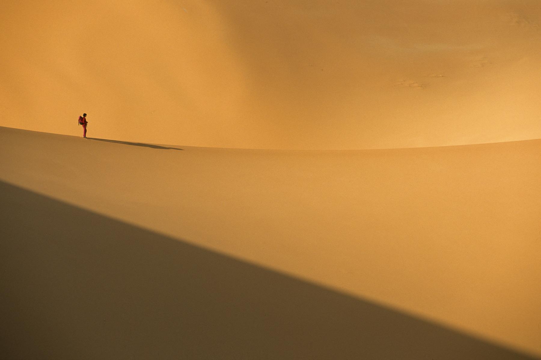 Femme de profil (silhouette rouge) progressant sur la crête d’une dune (Erg Wankasa, Désert de l’Akakus, Lybie)